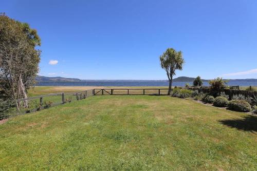 a large grassy field with a fence and a tree at Hannah's Bay Lakefront in Rotorua