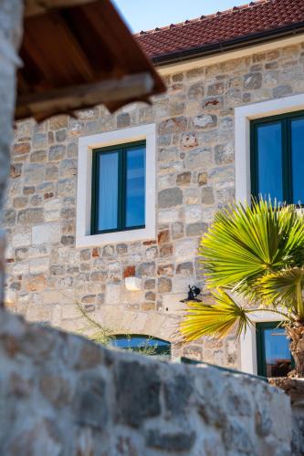 a stone house with windows and a palm tree at Villa Šjora - ''Autentic Dalmatian Stone Villa with Private Garden & BBQ'' in Vrboska