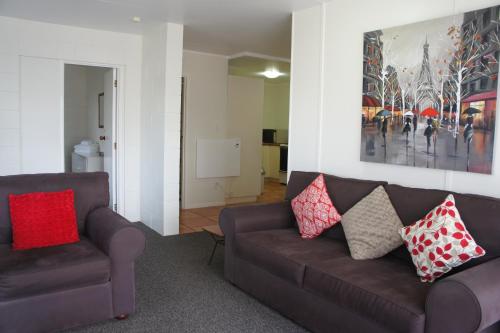 a living room with a brown couch and two chairs at Kerikeri Court Motel in Kerikeri