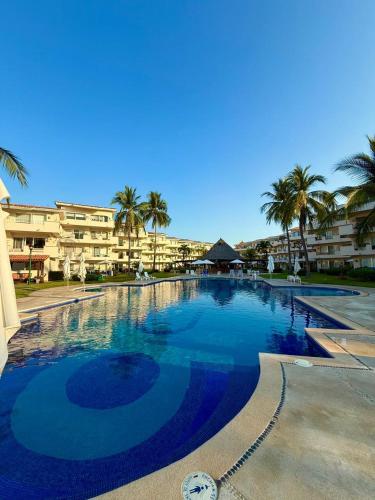 a large swimming pool with palm trees and buildings at Apartamento familiar con vista espectacular al mar in Ixtapa