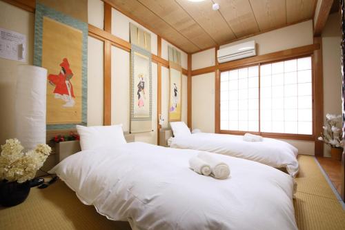 zwei Betten in einem Zimmer mit weißen Laken in der Unterkunft おまつりハウス in Osaka