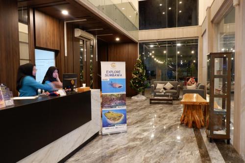 two women sitting at a counter in a lobby with a christmas tree at Grand Samota Hotel in Sumbawa Besar