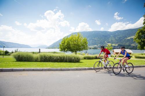 two people riding bikes down a road next to a lake at Wellness Landhaus Parth in Ossiach
