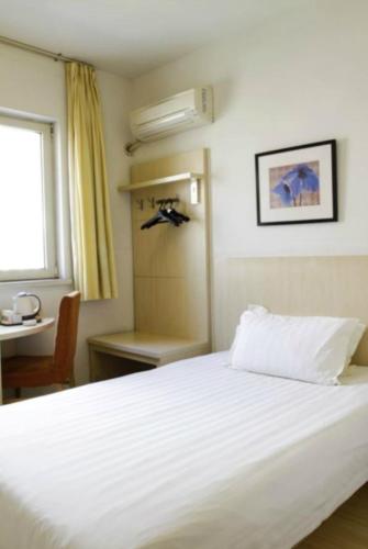 a bedroom with a white bed with a desk and a window at Jinjiang Inn Qingdao Bus Station in Qingdao