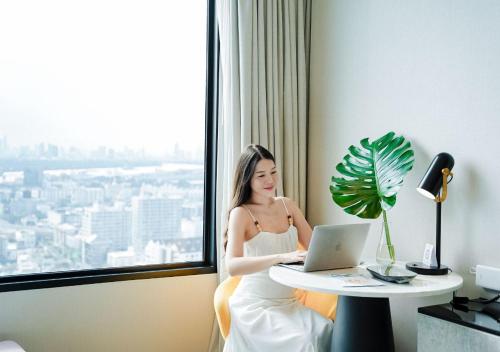 a woman sitting at a table with a laptop in a hotel room at Avani Sukhumvit Bangkok Hotel in Bangkok