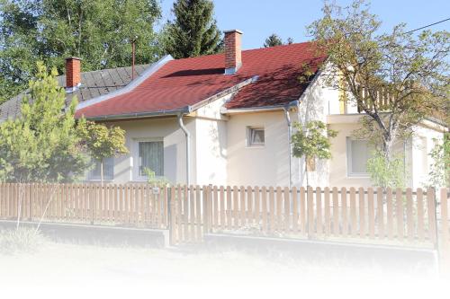 a white house with a fence and a red roof at Balaton Holiday Home in Balatonmáriafürdő