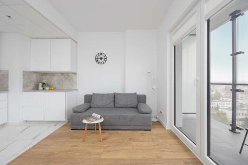 a living room with a gray couch and a kitchen at Apartments Kasprzaka near Metro Płocka with AC by Noclegi Renters in Warsaw