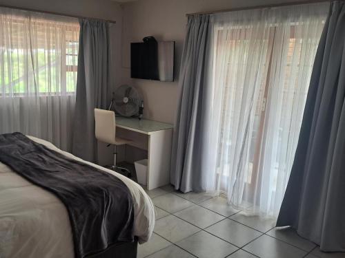 a bedroom with a bed and a desk and windows at Dolphin View Guesthouse in Jeffreys Bay