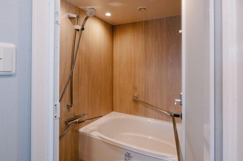 a bathroom with a tub and a wooden wall at Hotel Boston Plaza Kusatsu in Kusatsu