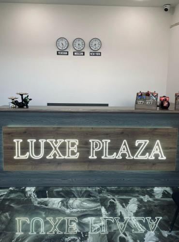 a sign that reads invoke plaza with clocks on the wall at Lux Plaza Hotel EVN airport in Arbatʼ