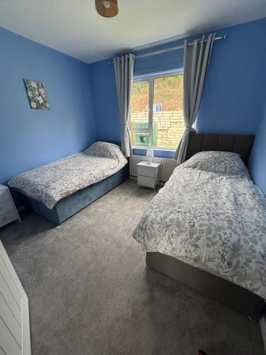 two beds in a bedroom with blue walls and a window at Christinas Cottage Downpatrick in Raholp