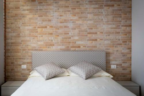 a bed with two pillows in front of a brick wall at Foresteria Lombarda GELSO BIANCO in Cogliate