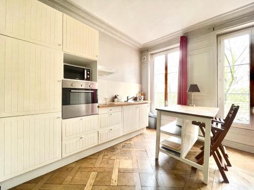une cuisine avec des armoires blanches, une table et un micro-ondes dans l'établissement Charming Haussmannian Apartment HyperCentre, à Rouen