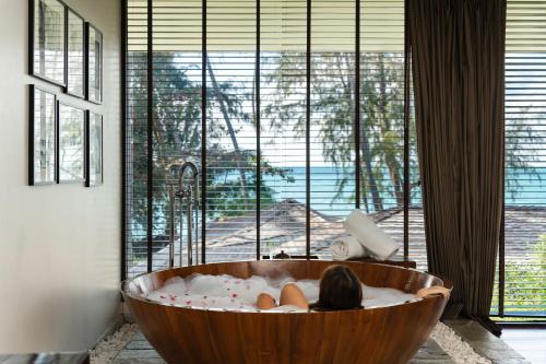 a woman laying in a wooden tub in a room with a window at Nikki Beach Resort & Spa Koh Samui in Lipa Noi