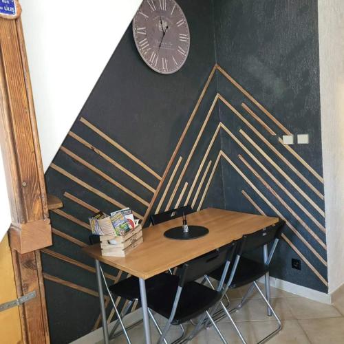 une table en bois avec des chaises et une horloge sur un mur dans l'établissement Lilas, à Saint-Bonnet-en-Champsaur