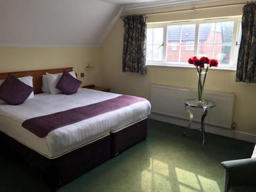 a bedroom with a bed with a vase of flowers on a table at Harefield Manor Hotel in Romford