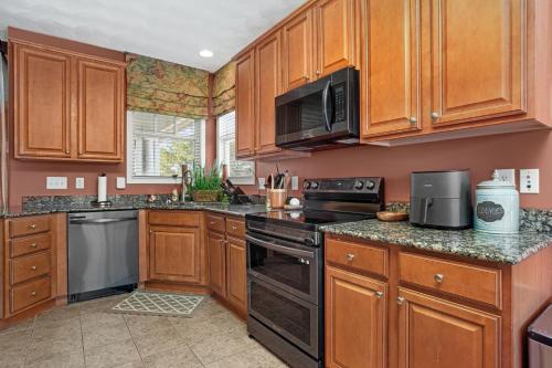 a kitchen with wooden cabinets and black appliances at Isla Villa - Comfortable Bay Creek townhome with pools & golf! in Cape Charles