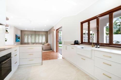 a kitchen with white cabinets and a living room at Casa Del Sol Palm Cove in Palm Cove
