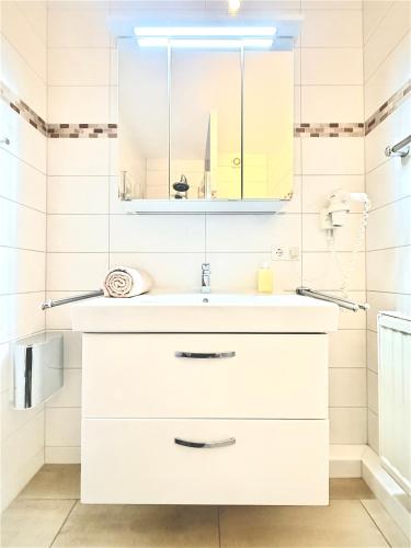 a white bathroom with a sink and a mirror at Duhnerherz Bestlage im Zentrum,am Strand Duhnen, Balkon mit Meerblick,Wlan Parkplatz und Fahrradabstellraum Bettwäsche und Handtücher inkl in Cuxhaven