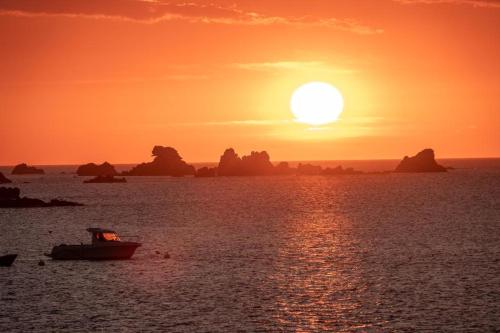 a boat in the water with a sunset in the ocean at Villa le Nid Des Dunes & Spa 2 gîtes écologiques in Santec