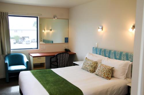 a hotel room with a bed and a desk and a window at Bella Vista Motel Mosgiel in Mosgiel