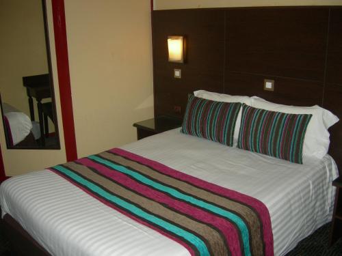 a bed in a hotel room with a striped blanket on it at Hôtel du Val de Seine in Mantes-la-Jolie
