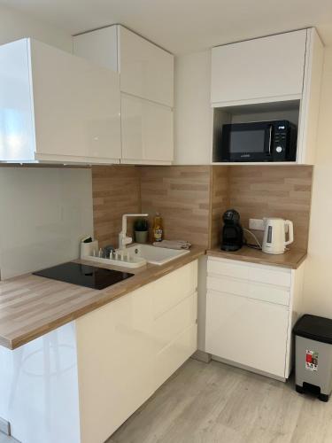 une cuisine avec des armoires blanches, un évier et un micro-ondes dans l'établissement Cozy studio Carnon Plage, à Mauguio