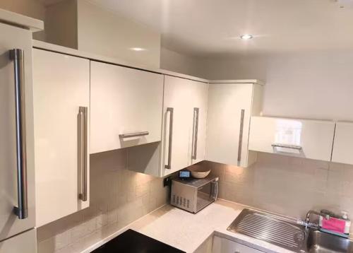 a kitchen with white cabinets and a microwave at Room with private bathroom, Near Heathrow Airport, Tube Station, Shops, Cinema in shared flat in Hounslow