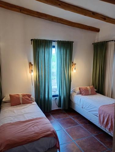 two beds in a room with green curtains and a window at La escondida las siringuillas in Tafí del Valle