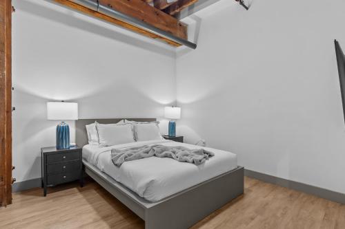 a white bedroom with a bed and a nightstand at Premier Downtown Loft, Steps to Arch & Convention Center in Saint Louis