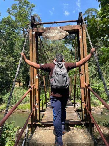 a man with a backpack crosses a wooden bridge at Rainforest River Bay in Deniyaya