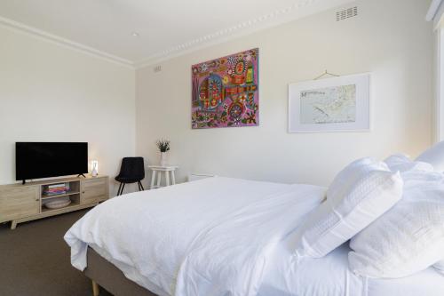 a white bedroom with a bed and a tv at Balcombe Retreat Mornington in Mornington