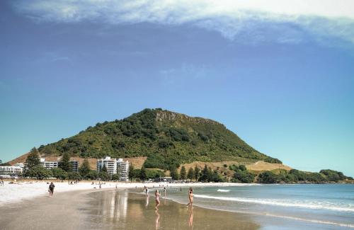 a group of people on a beach with a mountain at Oceanside Bliss - Absolute Beachfront - Uninterrupted Ocean Views with Pool in Mount Maunganui