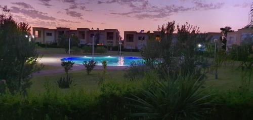 a swimming pool in the middle of a park at sunset at Duplex Reposant avec piscine au Andalines Golf Royal Fès in Dar Ito Lahssene