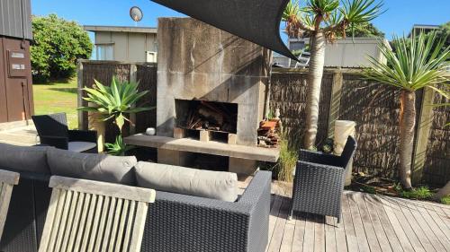 a patio with a fireplace and chairs and a fire pit at Beachfront Sunset Bach in Piha