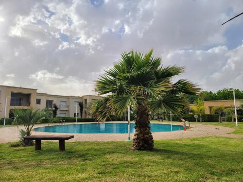 a palm tree and a bench next to a pool at Duplex Reposant avec piscine au Andalines Golf Royal Fès in Dar Ito Lahssene