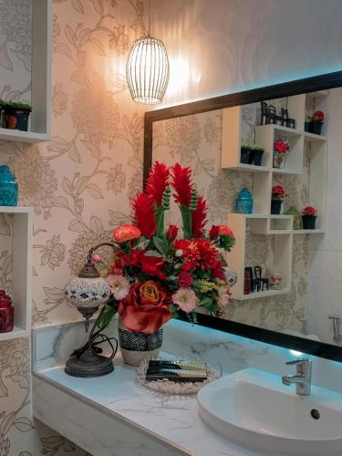 Un lavabo de baño con espejo y un jarrón con flores rojas. en Toffee Staycation, en Tagaytay