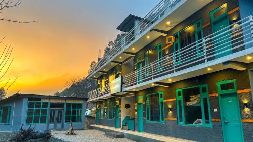 a building with green doors and a sunset in the background at Traverse Hostel Kasol in Kasol