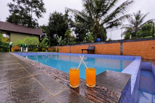 two glasses of orange juice sitting next to a swimming pool at sky blue villa in Vythiri