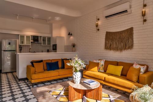 a living room with yellow couches and a table at La Masillia, 2 BHK with Private Pool, 15 mins from Morjim Beach, Wifi, Peaceful location, Kitchen, Security, Patio in Siolim