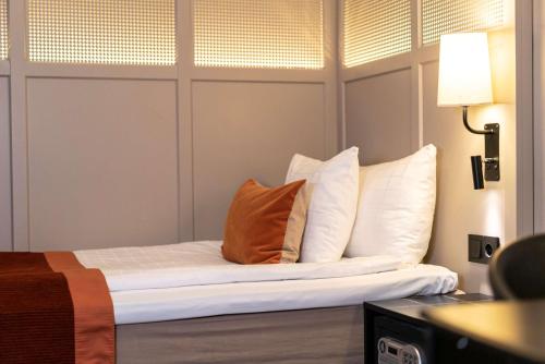 a bed with white pillows and an orange pillow at Scandic Grand Central in Stockholm