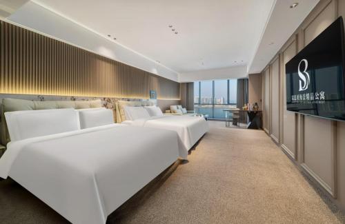 a hotel room with white beds and a television at 瑞思贝海景精品公寓 in Zhanjiang