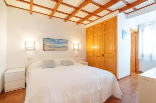 a white bedroom with a white bed and wooden ceilings at Oliver Villa con piscina y aire acondicionado! in Cala'n Bosch