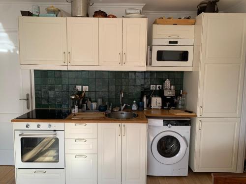 une cuisine avec des armoires blanches et une machine à laver dans l'établissement Sunny escape in Belleville, à Paris