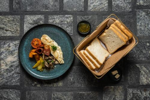 a plate of food with a sandwich and a basket of bread at Villa Mossa Ambalangoda Boutique villa in Ambalangoda