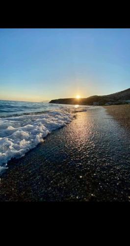 a beach with the sun setting over the water at MOUZOURAKIs APARTMENTS in Psari Forada