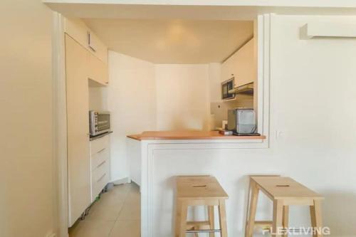 une petite cuisine avec un comptoir et deux tabourets dans l'établissement Flexliving - T2 - Guy de la Brosse, à Paris