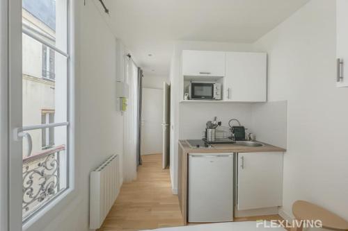 Elle comprend une petite cuisine avec des placards blancs et une fenêtre. dans l'établissement Flexliving - Studio - Étienne Marcel, à Paris