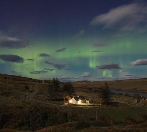 a house in a field with the aurora in the sky at The Old School House in Carbost