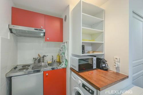 une petite cuisine avec des placards rouges et un four micro-ondes dans l'établissement Flexliving - Studio - Bauches, à Paris
